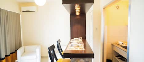 A compact kitchen with a marble countertop, a dining table set with plates and glasses, a hanging light fixture, and a white air conditioner on the wall.