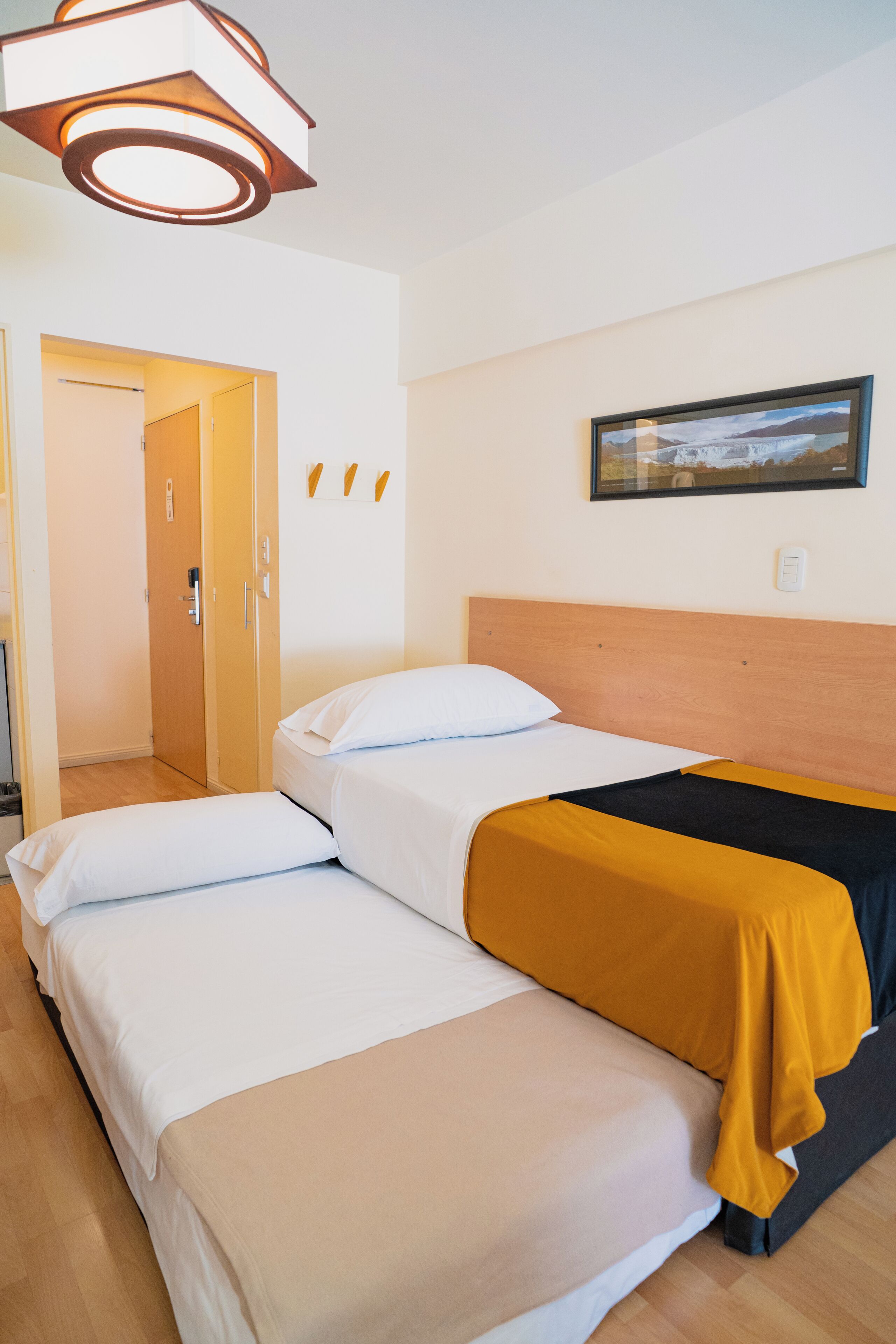 Ein Hotelzimmer mit Bett, Holz-Kopfteil, gerahmtem Bild an der Wand und einer Tür zu einem anderen Raum.