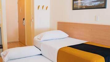 Habitación de hotel con cama, cabecera de madera, un cuadro enmarcado en la pared y una puerta que da a otra habitación.
