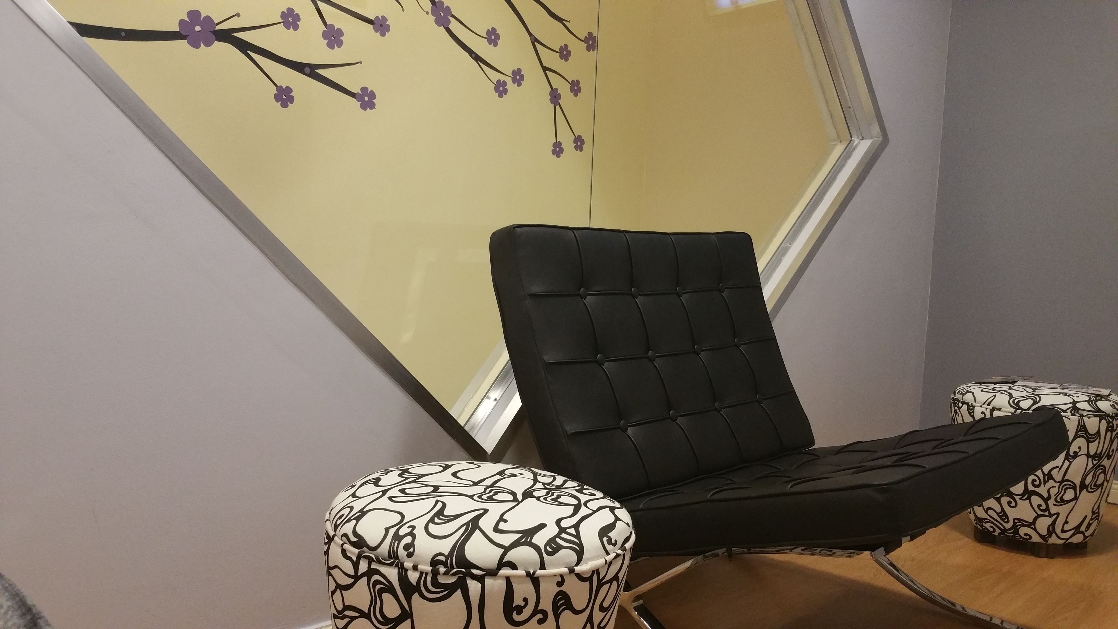 A modern room with a black chair and ottoman, a large window with a view, and a wall with a floral design.
