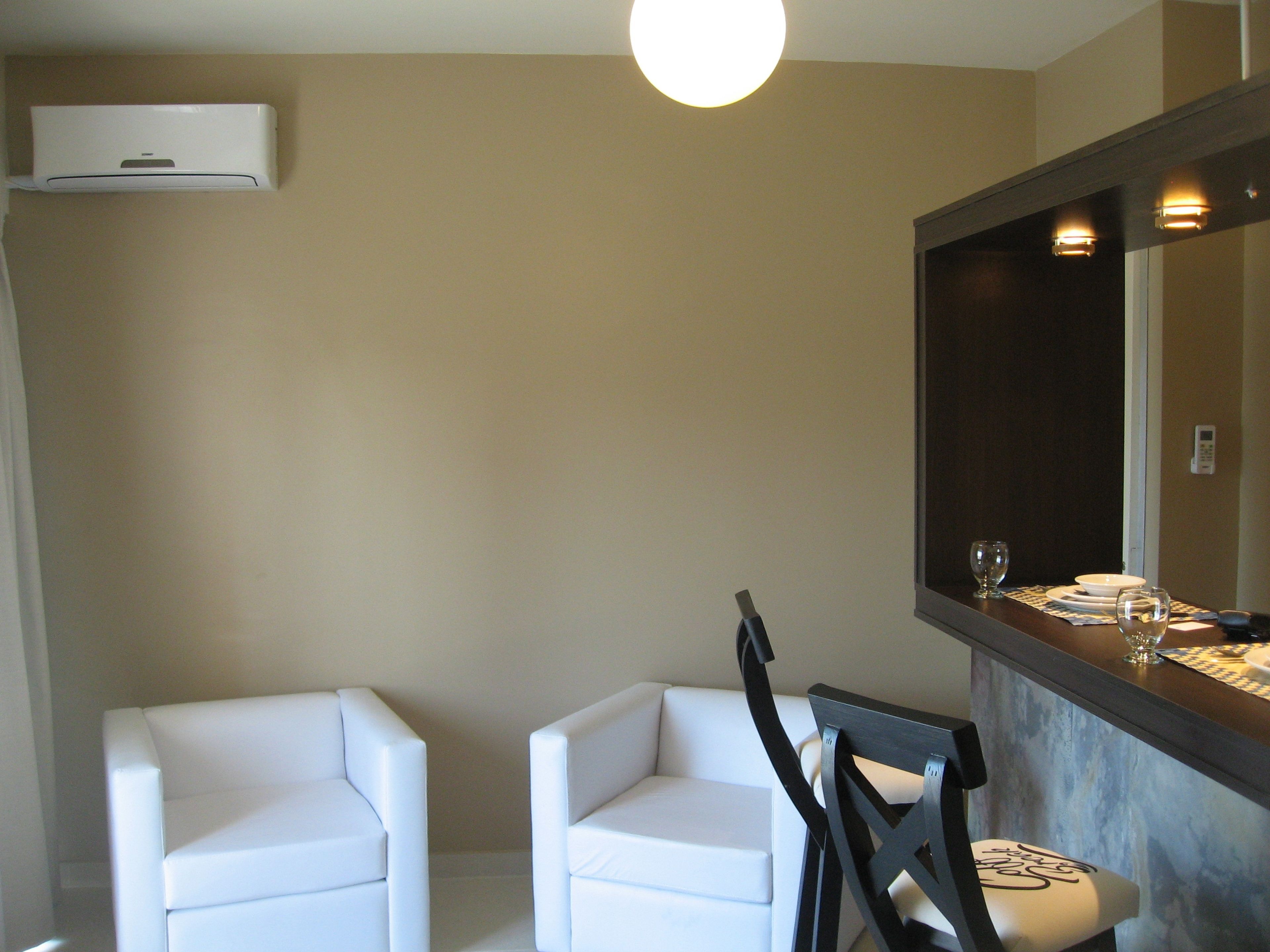 A modern, minimalist bathroom with two white chairs, a dark wooden chair, and a large mirror above a countertop.