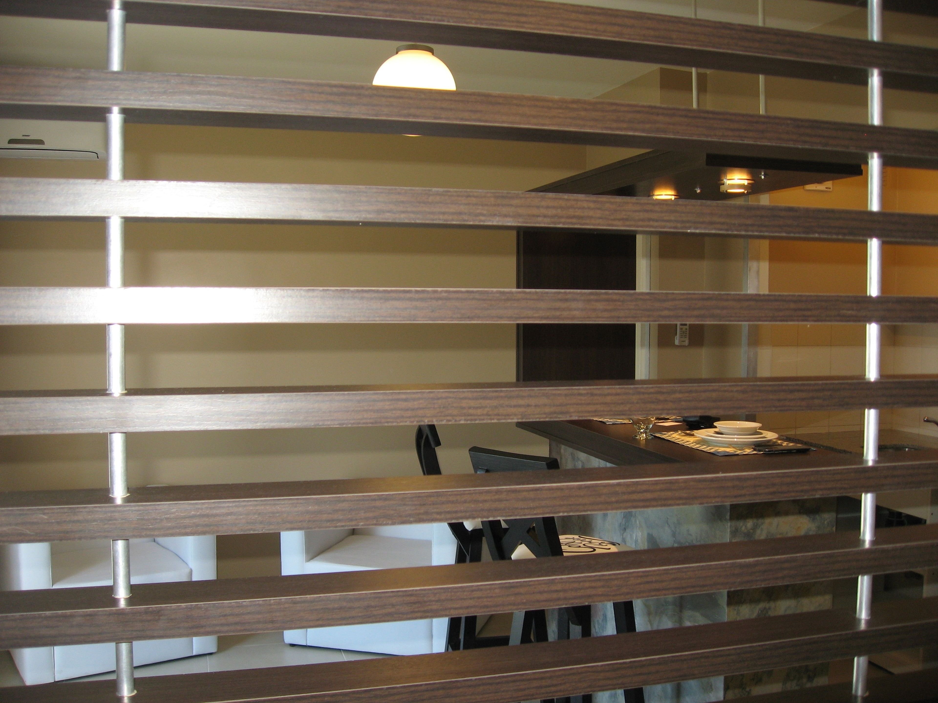 Una habitación con un separador de madera, una mesa de comedor con sillas y una lámpara en el techo.
