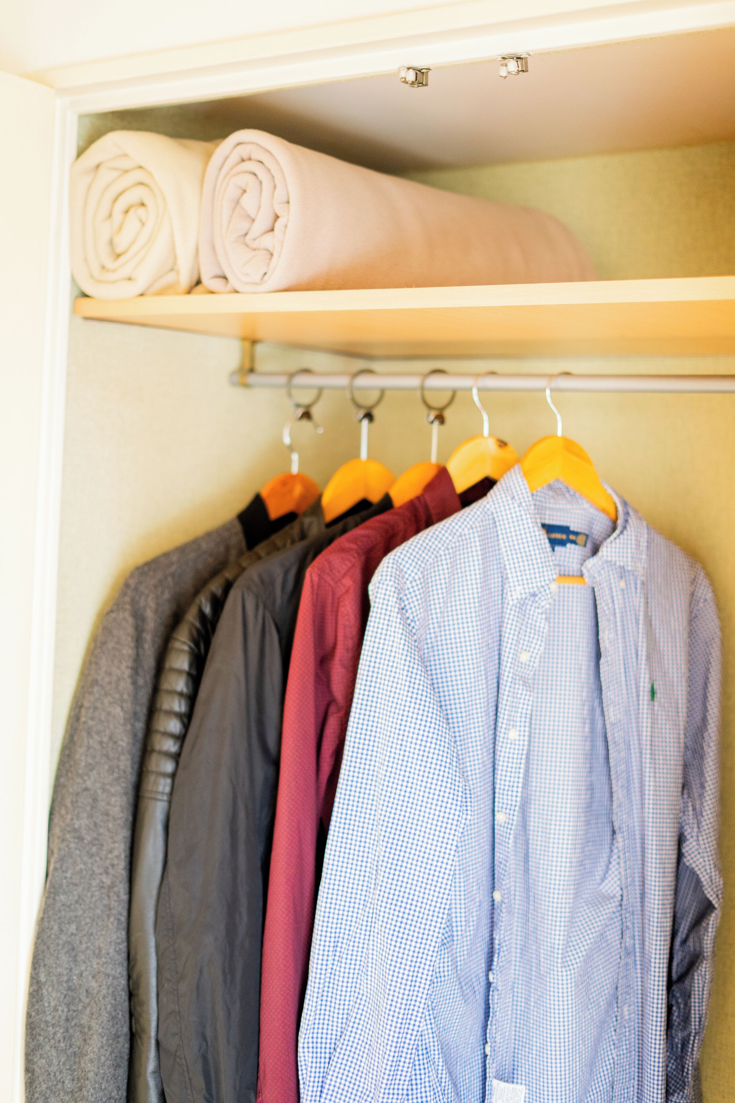 A closet with neatly folded clothes on the top shelf and a selection of shirts hanging below.
