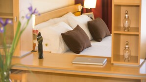 Una habitación de hotel con una cama, almohadas, una mesita de noche con una lámpara, un ordenador portátil y una botella decorativa en un estante.