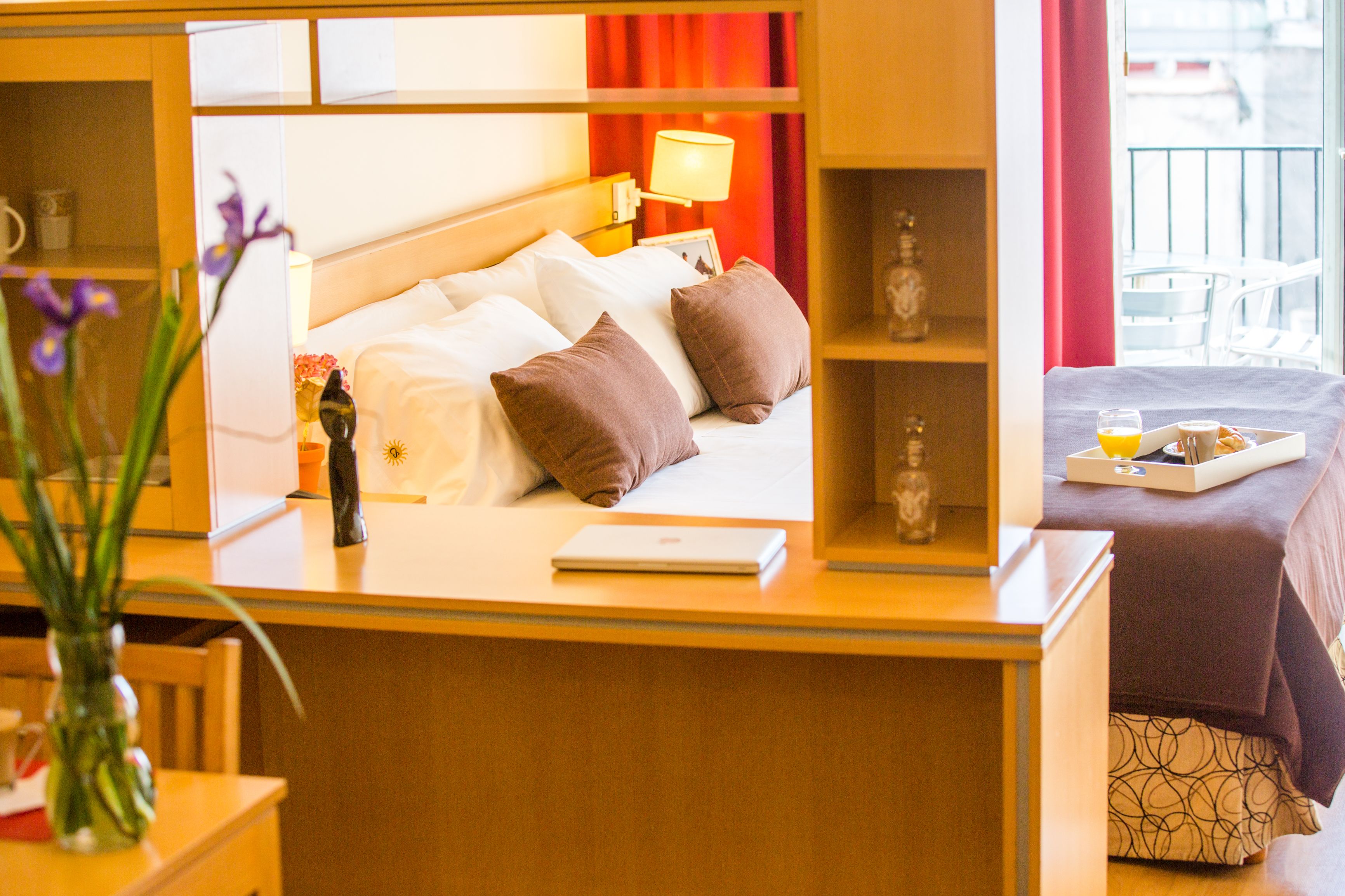 Quarto de hotel com uma cama, uma secretária com um laptop, um tabuleiro com itens de pequeno-almoço e vista para a varanda exterior.