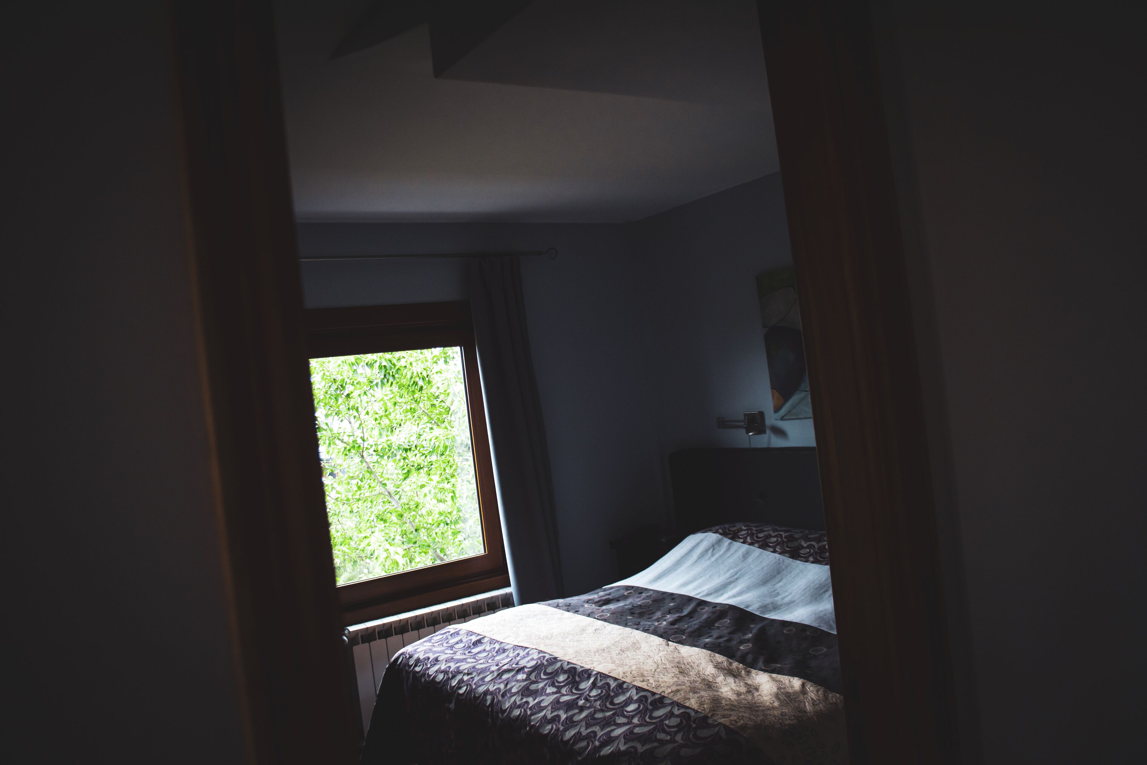 A dimly lit room with a bed, a window, and a nightstand.