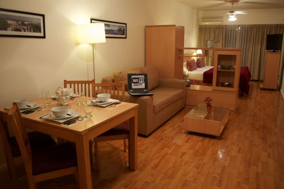Habitación de hotel con una mesa de comedor preparada para dos personas, un sofá, una pequeña mesa de centro y un televisor.