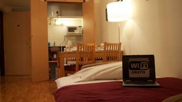 Habitación de hotel con cama, escritorio con una laptop mostrando “WiFi Gratis”, una silla, una mesa y un microondas al fondo.