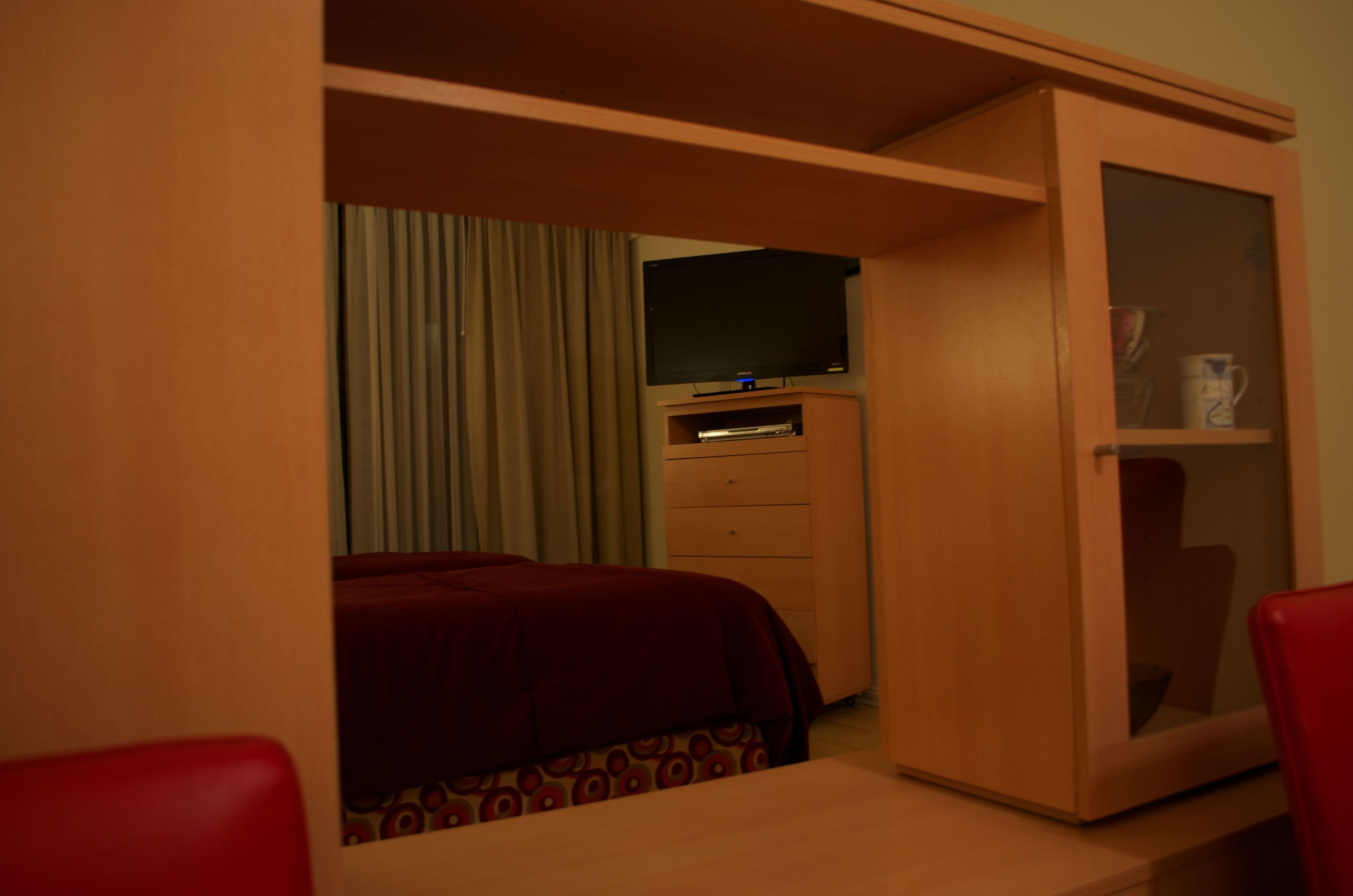 A hotel room with a bed, a television on a stand, a wooden wardrobe, and a red chair.