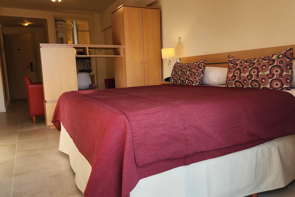 Una habitación de hotel con una cama grande, un armario, un escritorio y una silla.