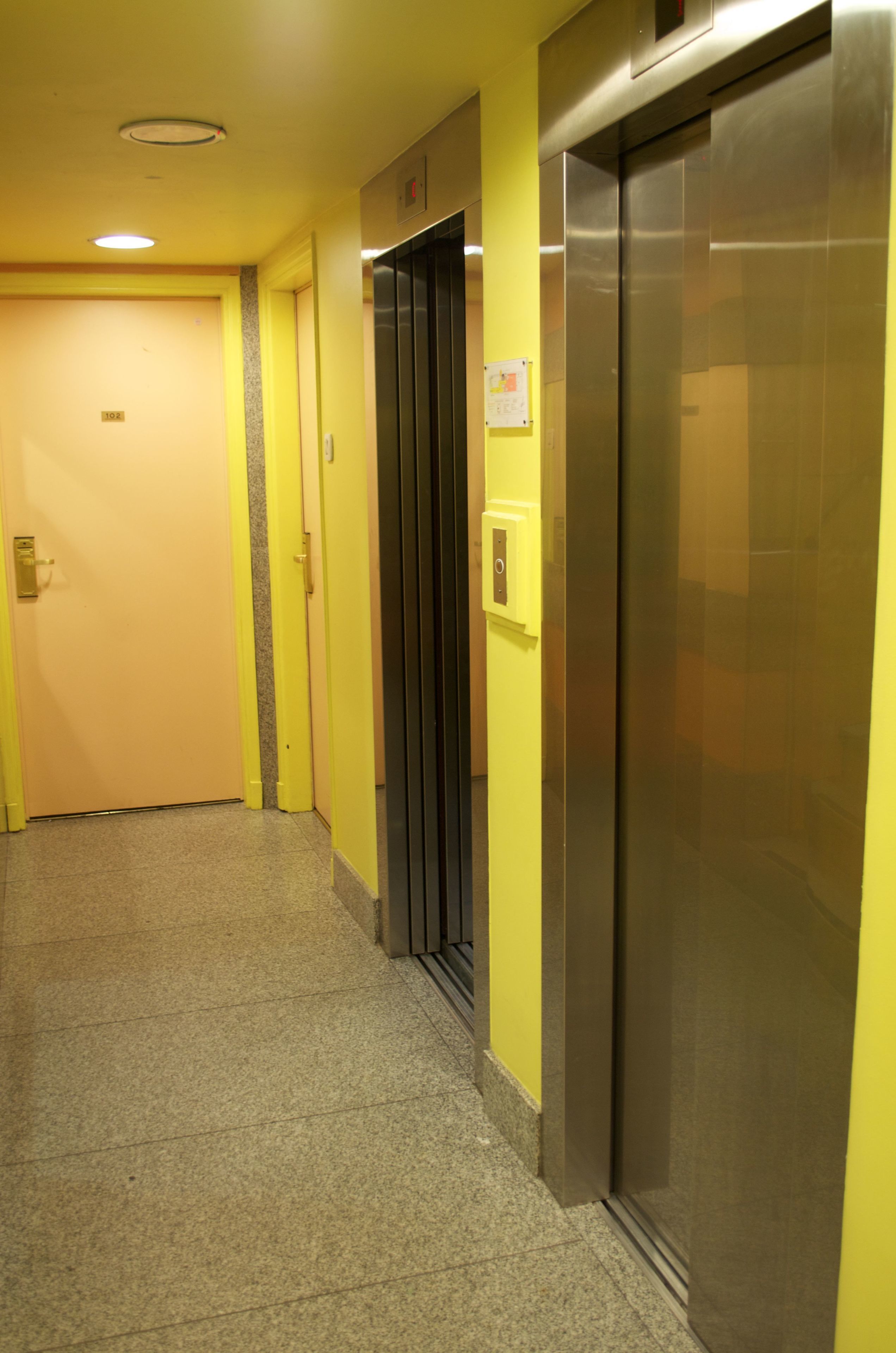 Un pasillo con una puerta, un ascensor y un panel de control en la pared.