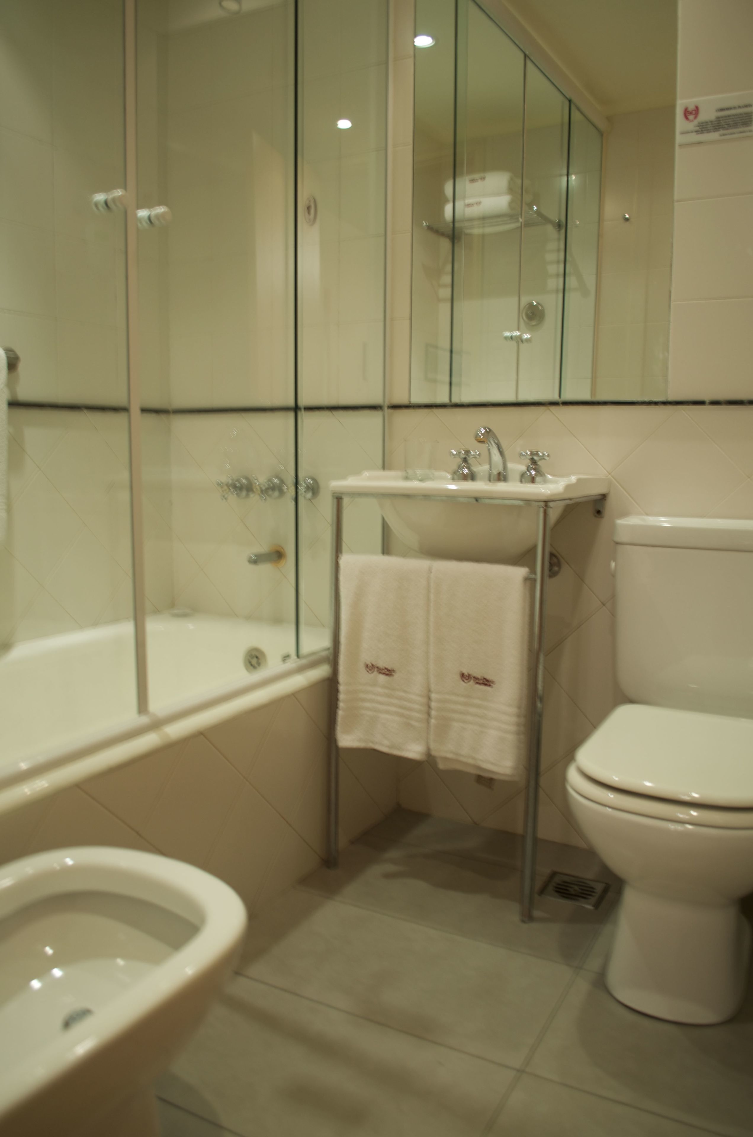 Une salle de bain avec une douche à parois de verre, un lavabo avec un miroir, des toilettes et un bidet.