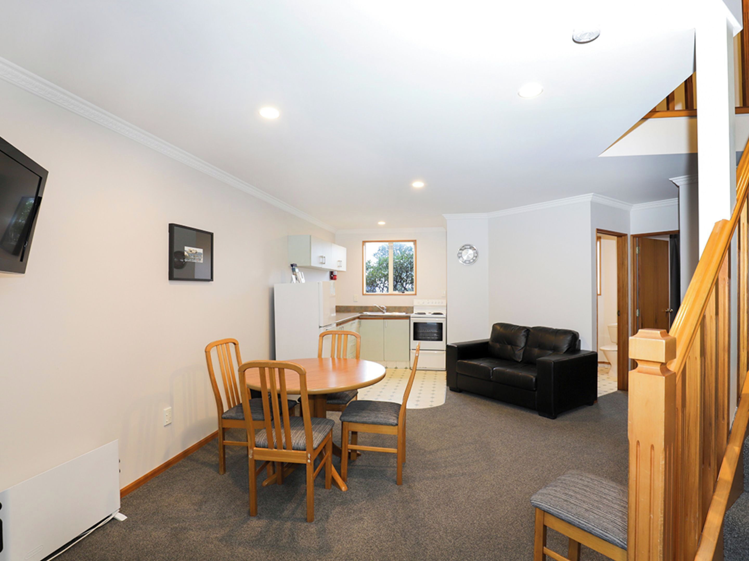 A compact living space with a dining area, kitchen, and a black leather sofa.