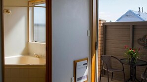 A bathroom with a bathtub, a toilet, and a sink. There is a window with a view of a house and a garden. - ASURE Chelsea Gateway Motor Lodge (Westport)
