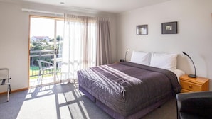 A hotel room with a bed, a nightstand, a chair, and a view of the outside. - ASURE Chelsea Gateway Motor Lodge (Westport)