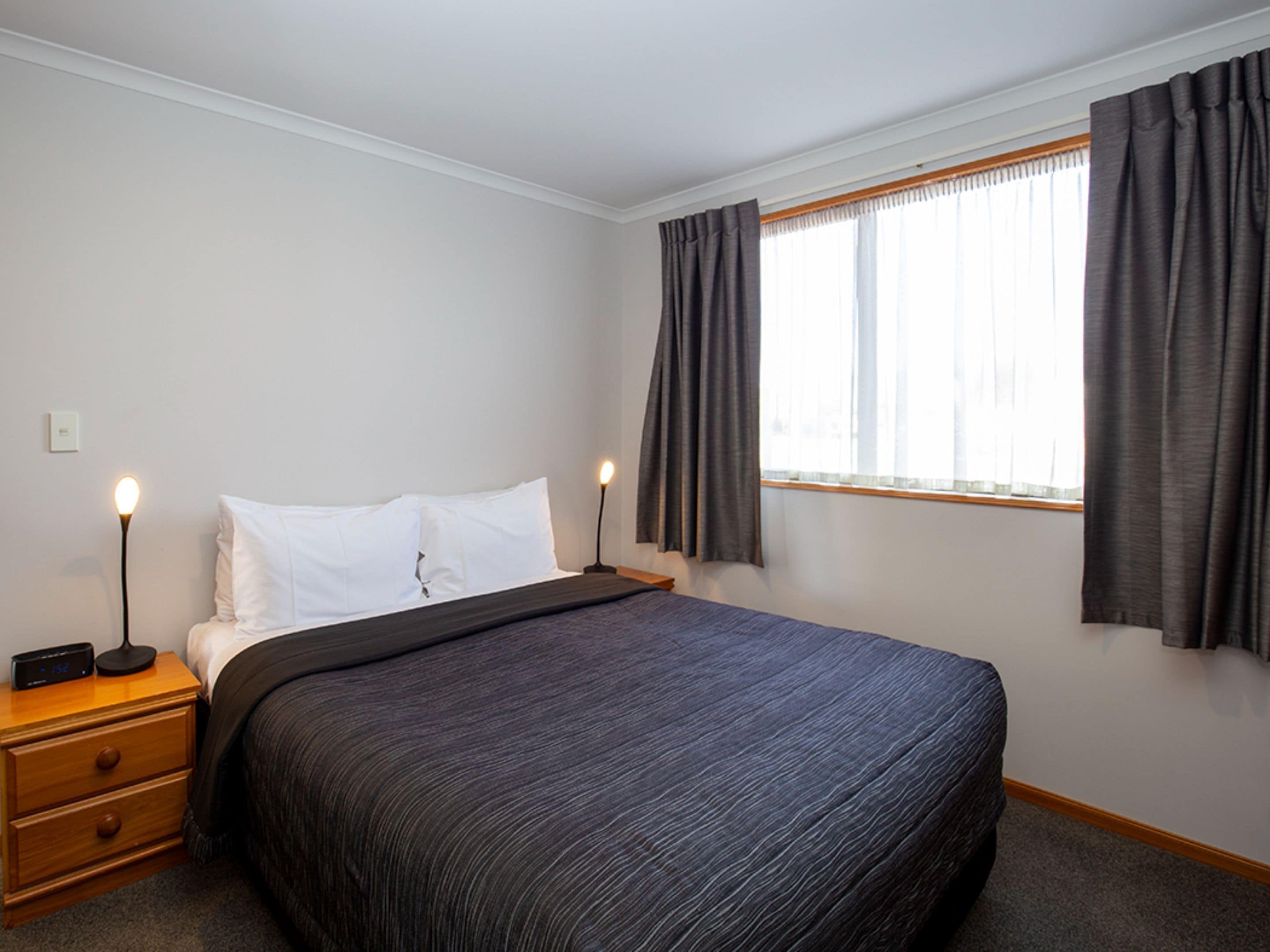 A neatly arranged hotel room with a single bed, a bedside table with a lamp, and a window with curtains.