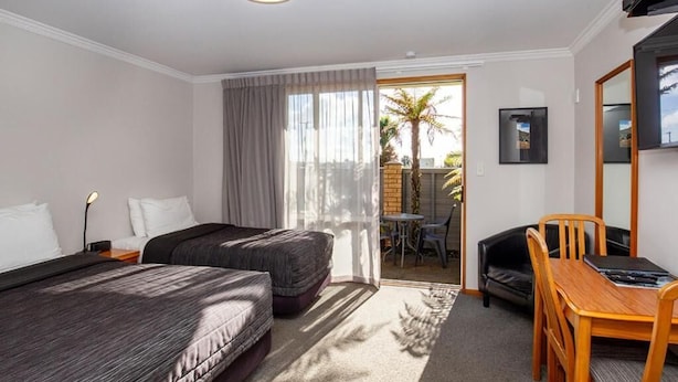 A hotel room with two beds, a desk, a chair, a TV, and a sliding door to an outdoor area with a table and chairs. - ASURE Chelsea Gateway Motor Lodge (Westport)