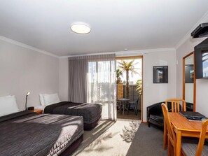 A hotel room with two beds, a desk, a chair, a TV, and a sliding door to an outdoor area with a table and chairs. - ASURE Chelsea Gateway Motor Lodge (Westport)