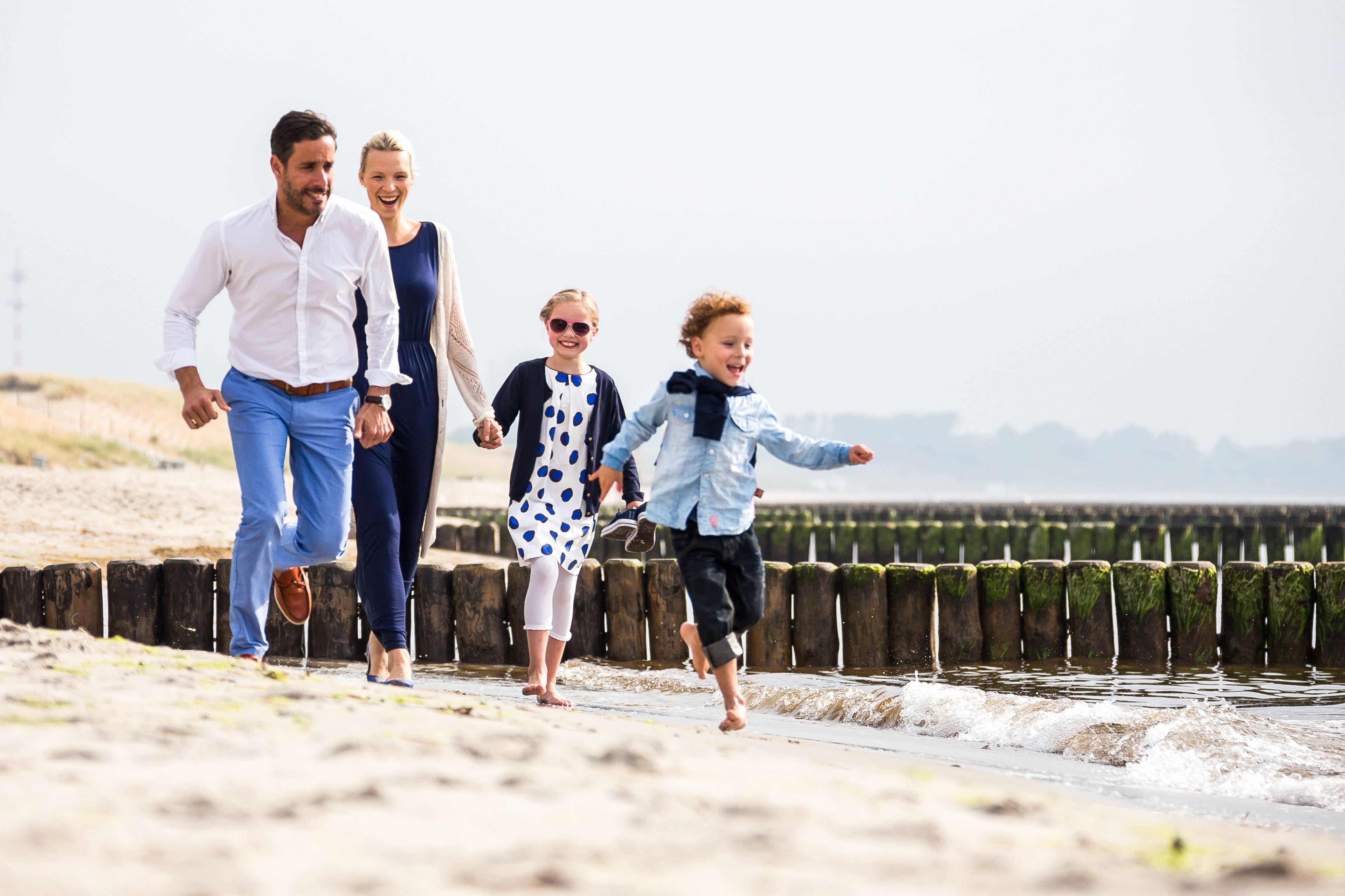 Una famiglia cammina lungo una spiaggia con una barriera di legno e l'oceano sullo sfondo.
