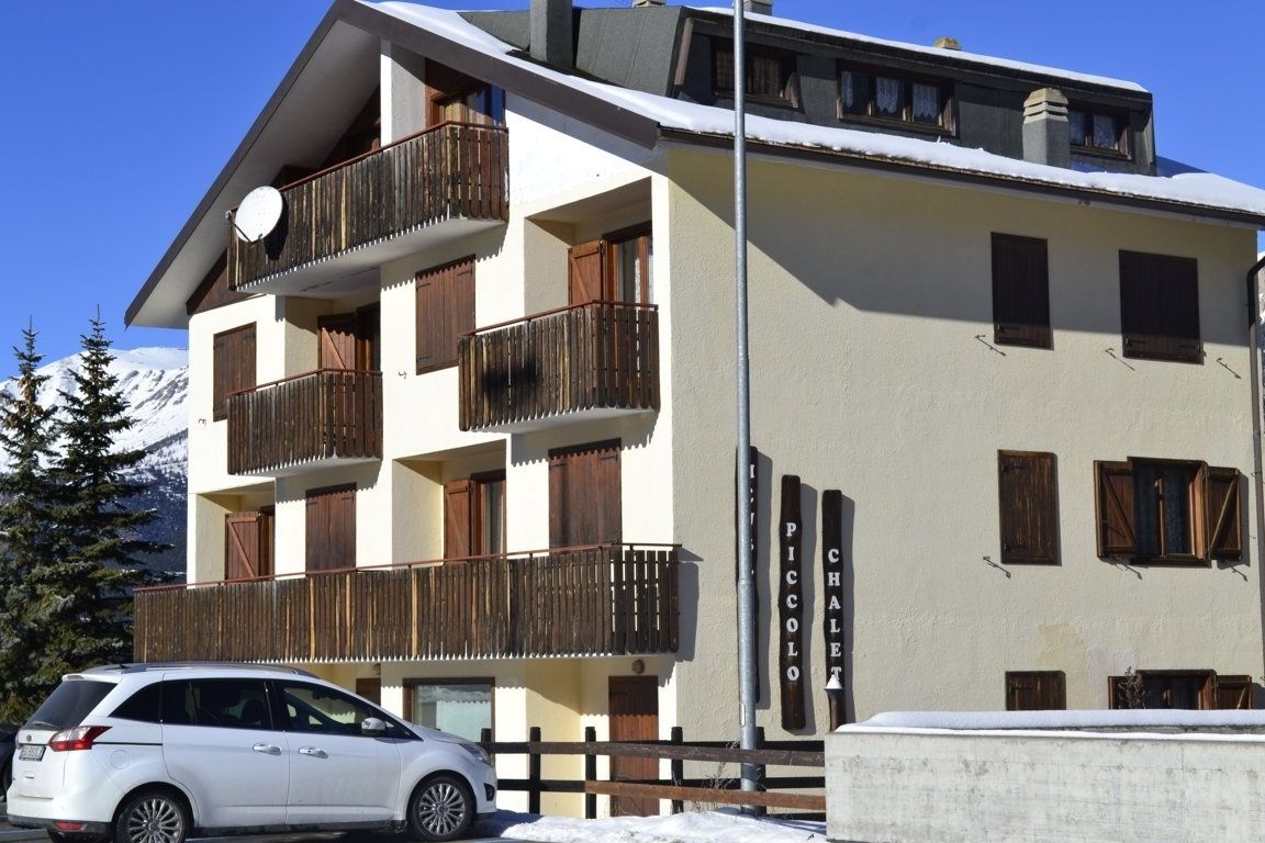 Ein mehrstöckiges Gebäude mit Balkonen, ein Auto davor und ein Schild mit der Aufschrift 'PICCOLO CHALET'.