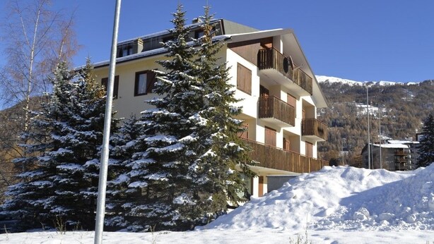A multi-story building with balconies, surrounded by snow-covered trees and a mountain backdrop. - Piccolo Chalet (Sauze d'Oulx)