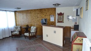 A living room with a wooden paneled wall, a television, a floral armchair, a small table, and a patterned rug. - Piccolo Chalet (Sauze d'Oulx)