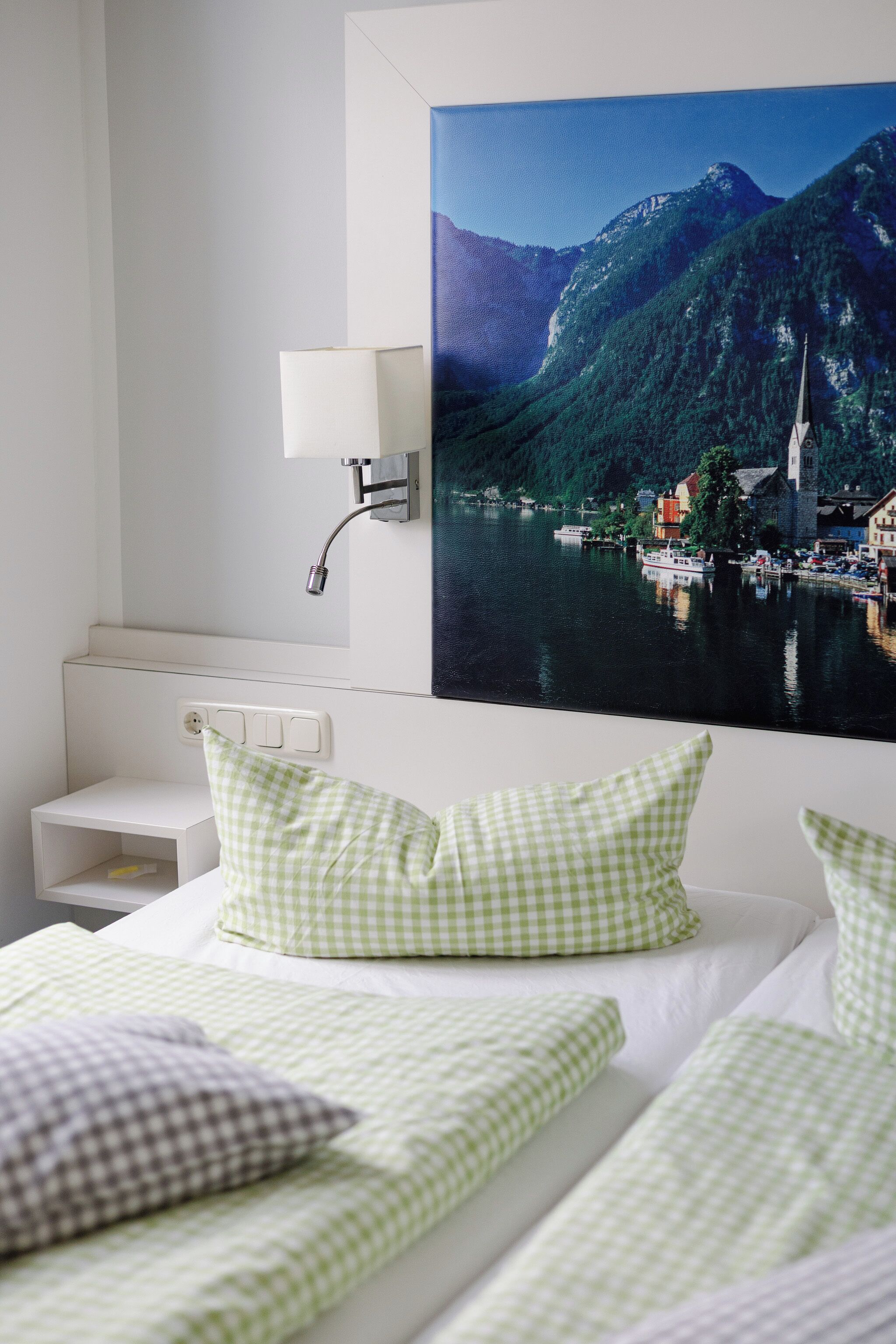 Ein Hotelzimmer mit Bett, Nachttisch, Lampe und einer großen Wandmalerei mit Landschaftsmotiv.