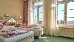 Habitación de hotel con dos camas, vistas a la ciudad a través de amplias ventanas y un radiador en el suelo.
