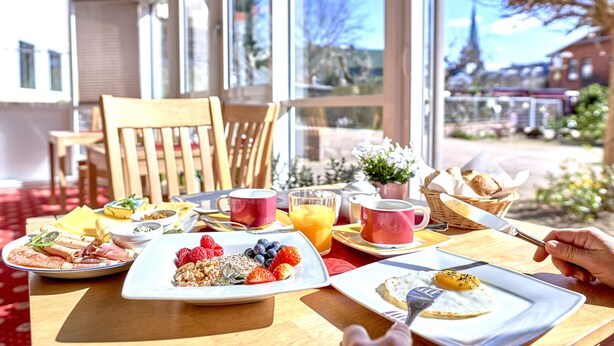 Una escena de desayuno con platos de comida, una taza de café y un vaso de jugo de naranja sobre una mesa.