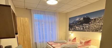 Habitación de hotel con cama, escritorio con teléfono, silla, ventana con cortinas y televisión de pared.