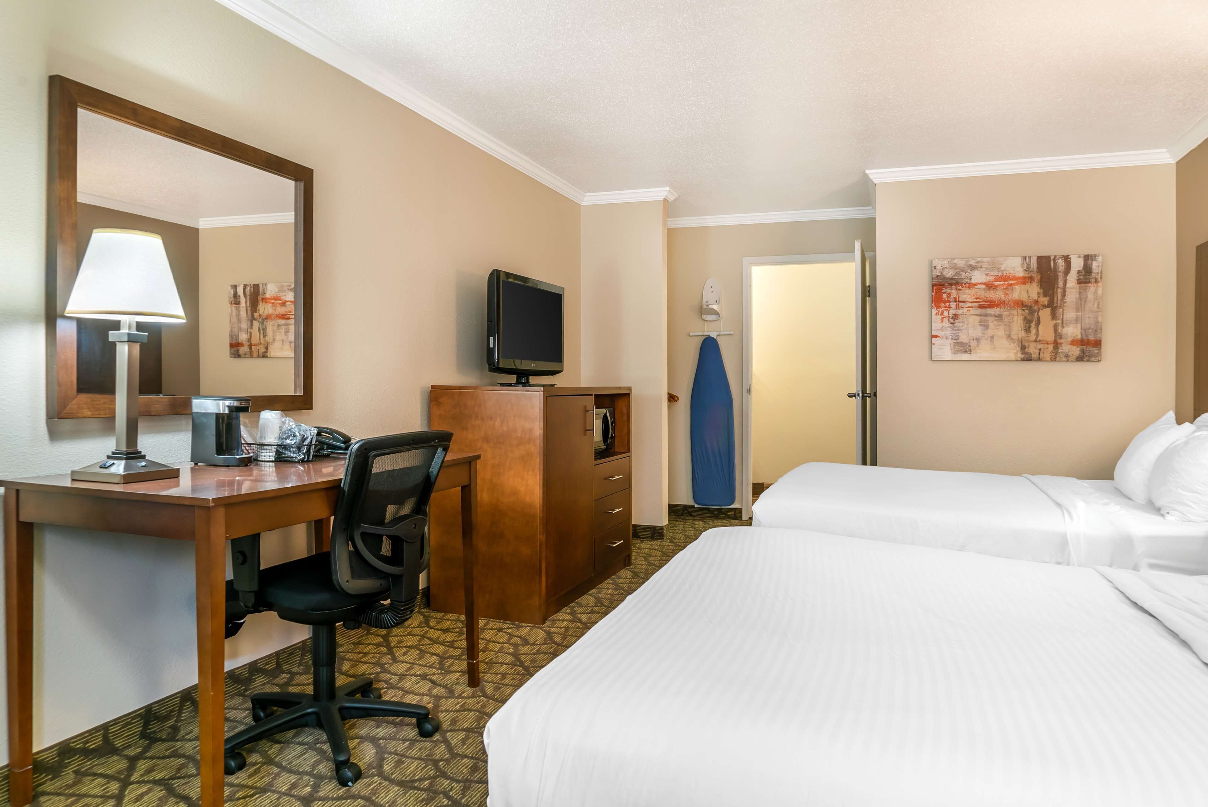 Habitación de hotel con cama, escritorio con silla, televisión, espejo y obras de arte en las paredes.