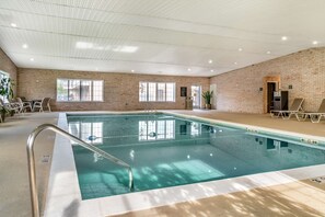 Ein Hallenbad mit Backsteinwand, einer Poolleiter und einem Sitzbereich mit Stühlen und einem Tisch.