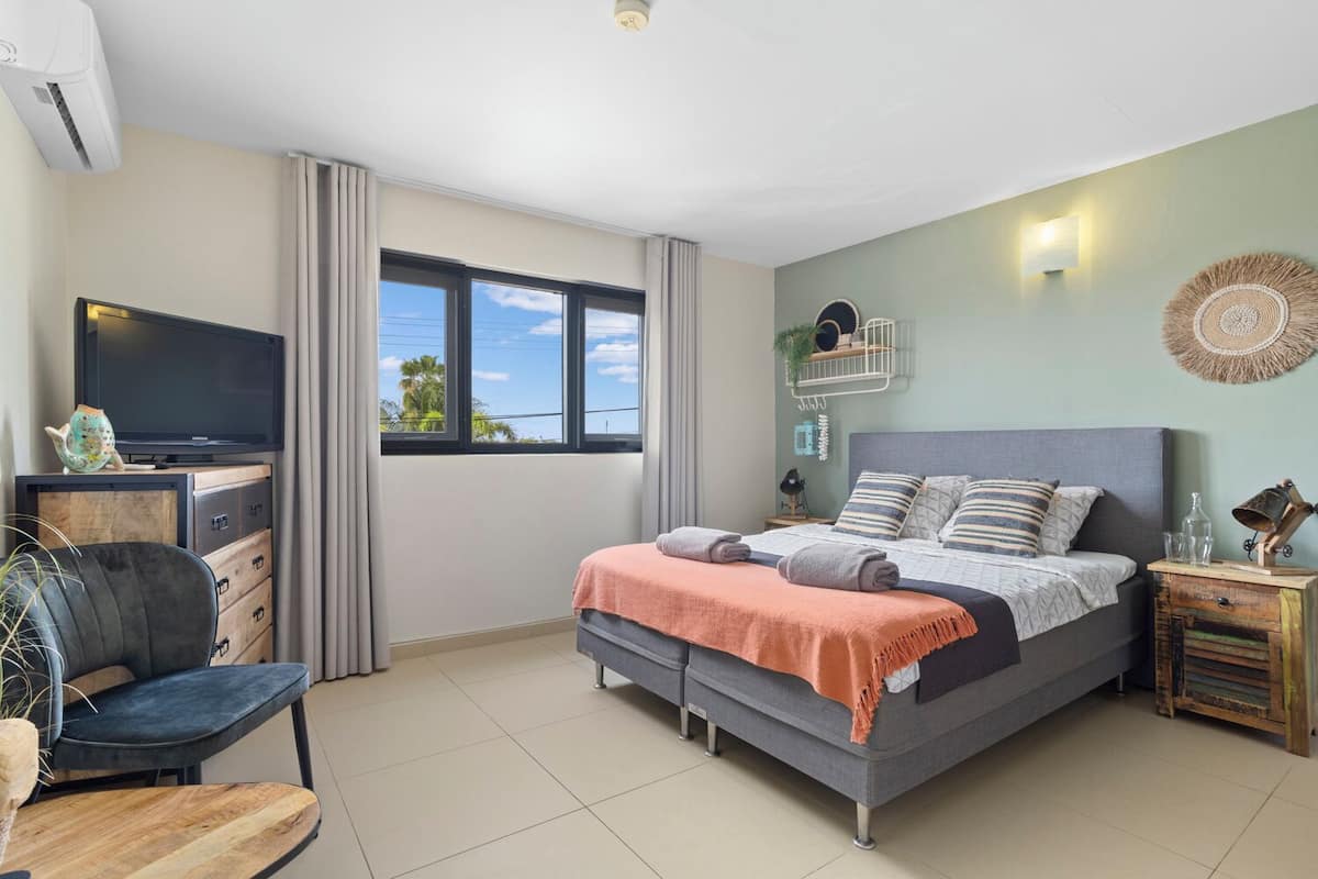 A bedroom with a bed, a desk with a TV, a chair, and a window.