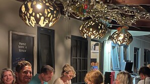 Un grupo de personas cenando en un restaurante con una decoración rústica, que incluye vigas de madera a la vista y lámparas colgantes.