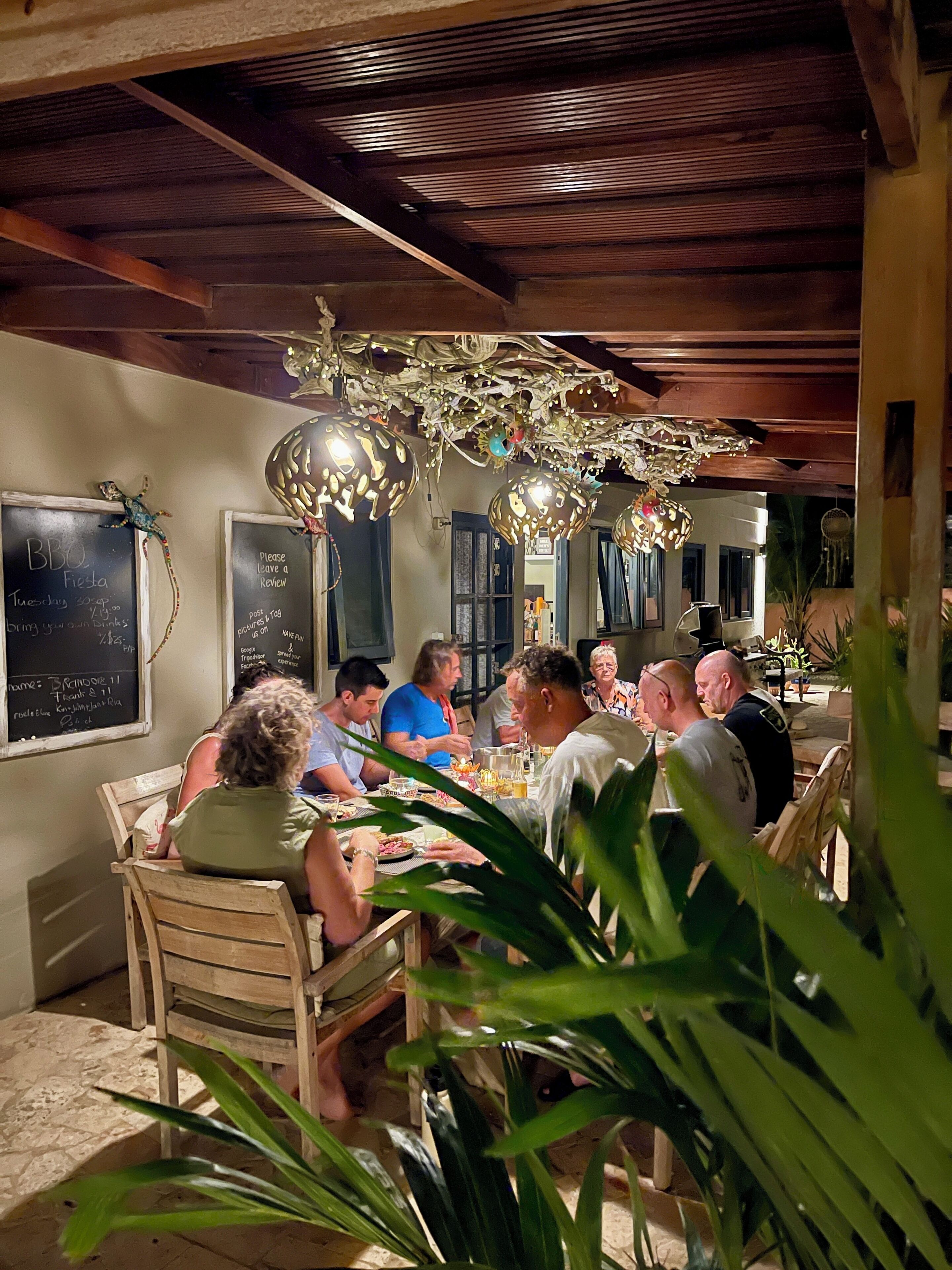 Un groupe de personnes est assis autour d’une table en bois, dans un décor rustique avec un plafond en bois et des lampes décoratives suspendues.