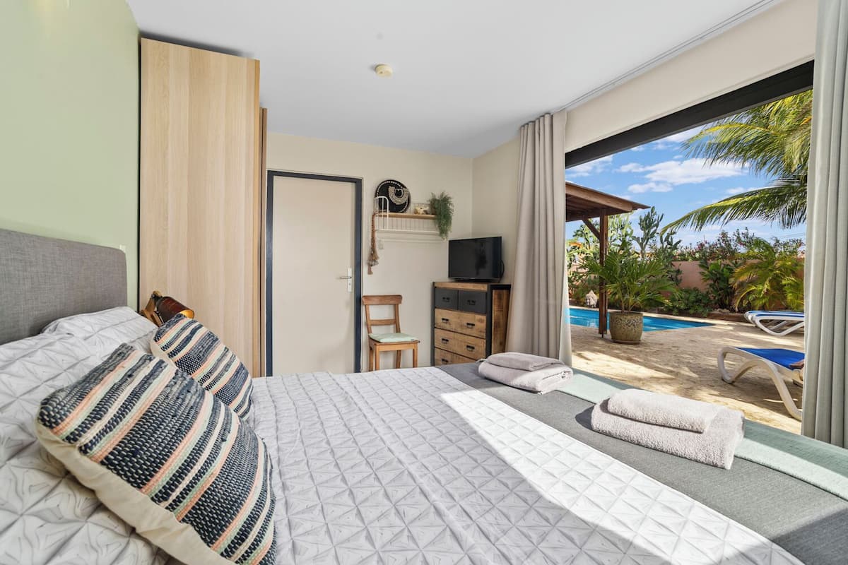 A bedroom with a large bed, a TV, a desk, and a view of a pool and outdoor area.