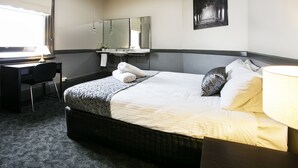 Une chambre d’hôtel avec un lit, un bureau, une chaise, un miroir et un tableau au mur.
