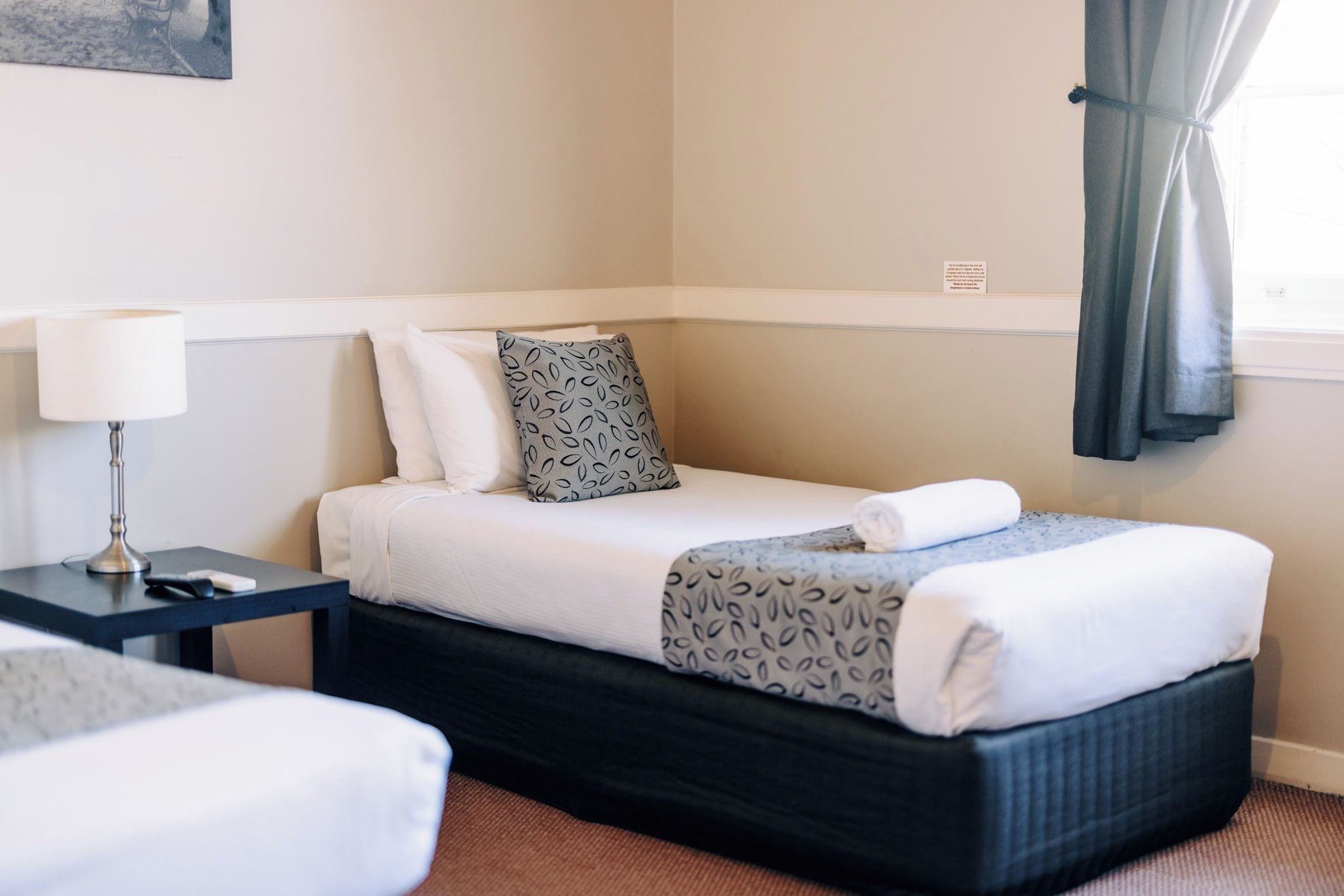 A hotel room with a bed, bedside table, lamp, and a window with curtains.
