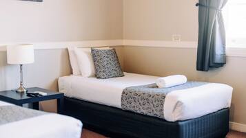 A hotel room with a bed, bedside table, lamp, and a window with curtains.