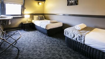 A hotel room with two beds, a desk with a chair, a small table with a lamp, and a TV mounted on the wall.