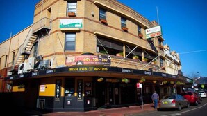 Un immeuble d’angle abritant un pub et un bistrot au rez-de-chaussée, caractérisé par une façade en briques et de nombreuses fenêtres.