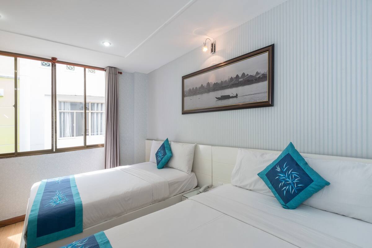 Ein Hotelzimmer mit zwei Betten, einem großen Fenster und einem gerahmten Bild an der Wand.