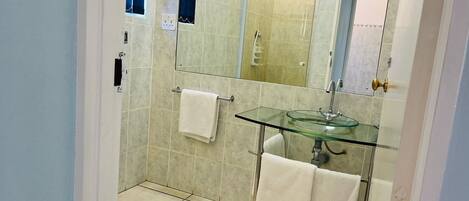 A bathroom with a glass sink, a mirror, and a shower area.