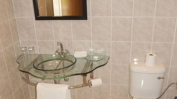 Casa de banho com lavatório de vidro, sanita e espelho sobre o lavatório.