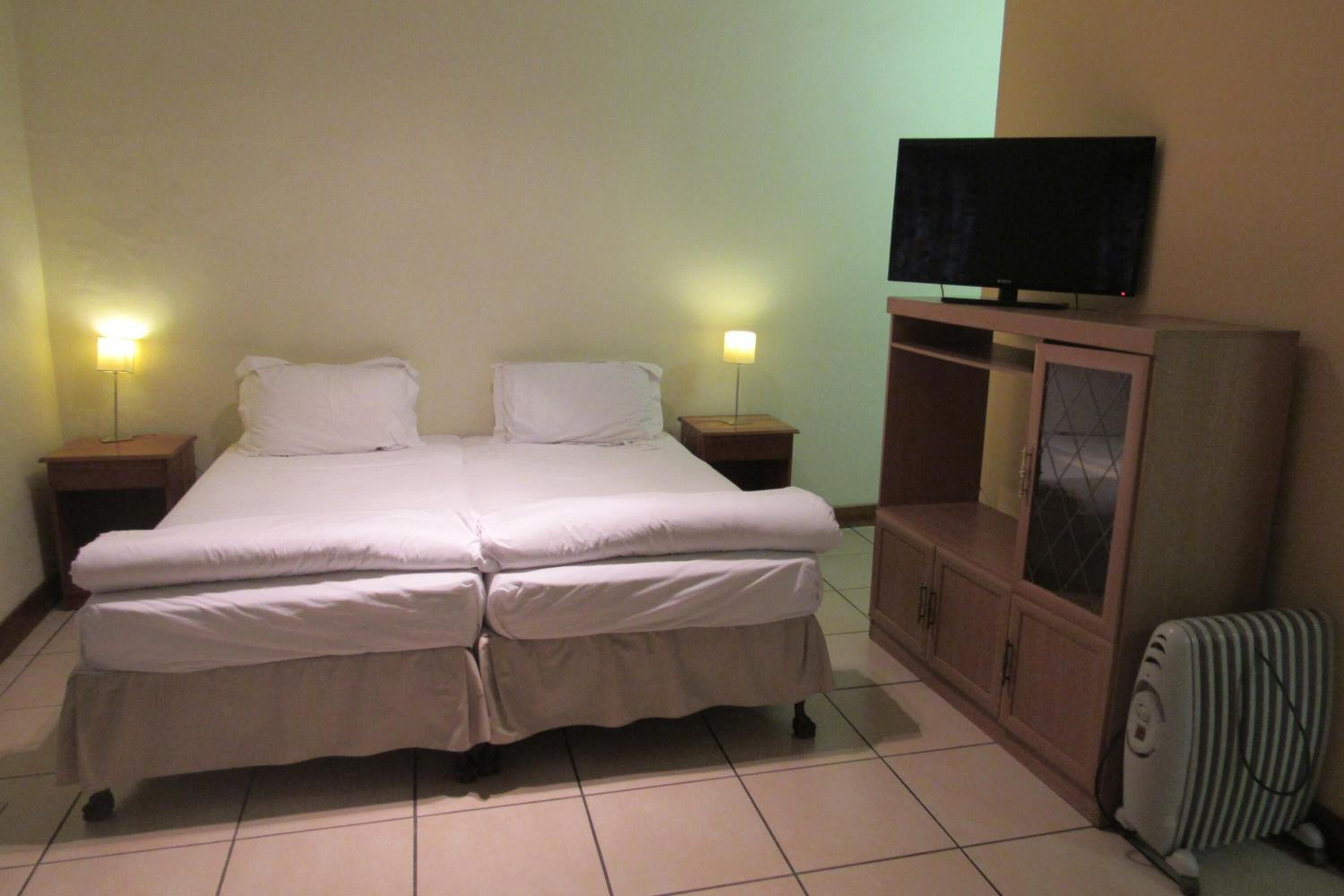 Una cama doble con dos almohadas, un televisor sobre un mueble bajo y dos lámparas de noche.