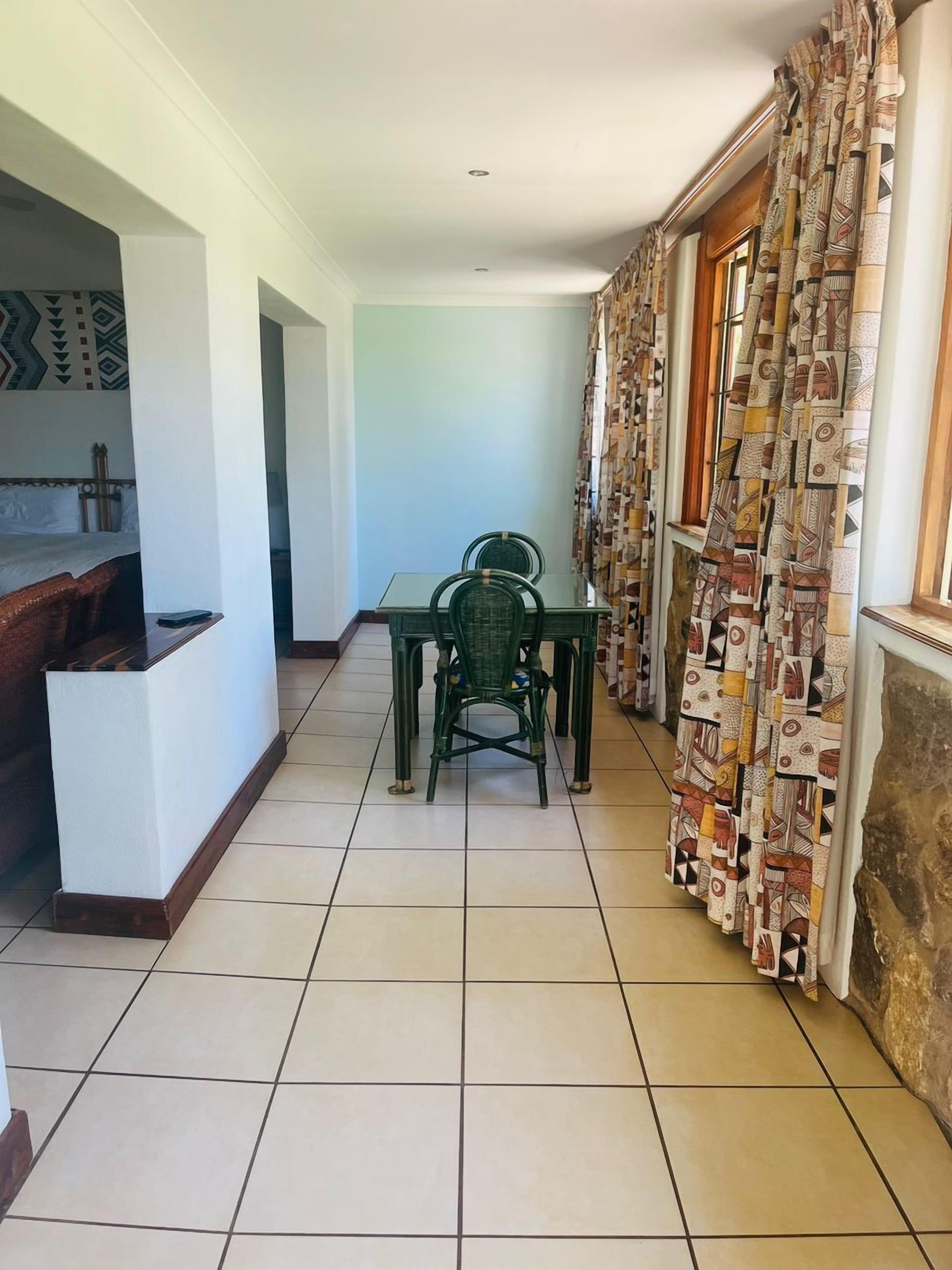Una habitación con una mesa de comedor y sillas, una cama con cabecera y cortinas estampadas.