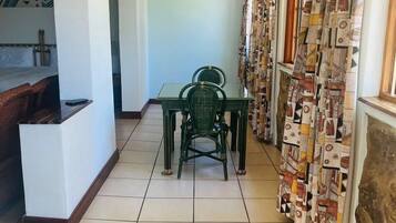 Una habitación con una mesa de comedor y sillas, una cama con cabecera y cortinas estampadas.