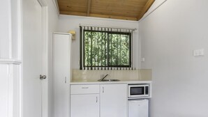 Una cocina compacta con armarios blancos, microondas y una ventana con reja de metal.