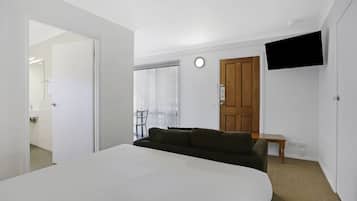 A bedroom with a large bed, a TV mounted on the wall, a wooden door, and a small table.