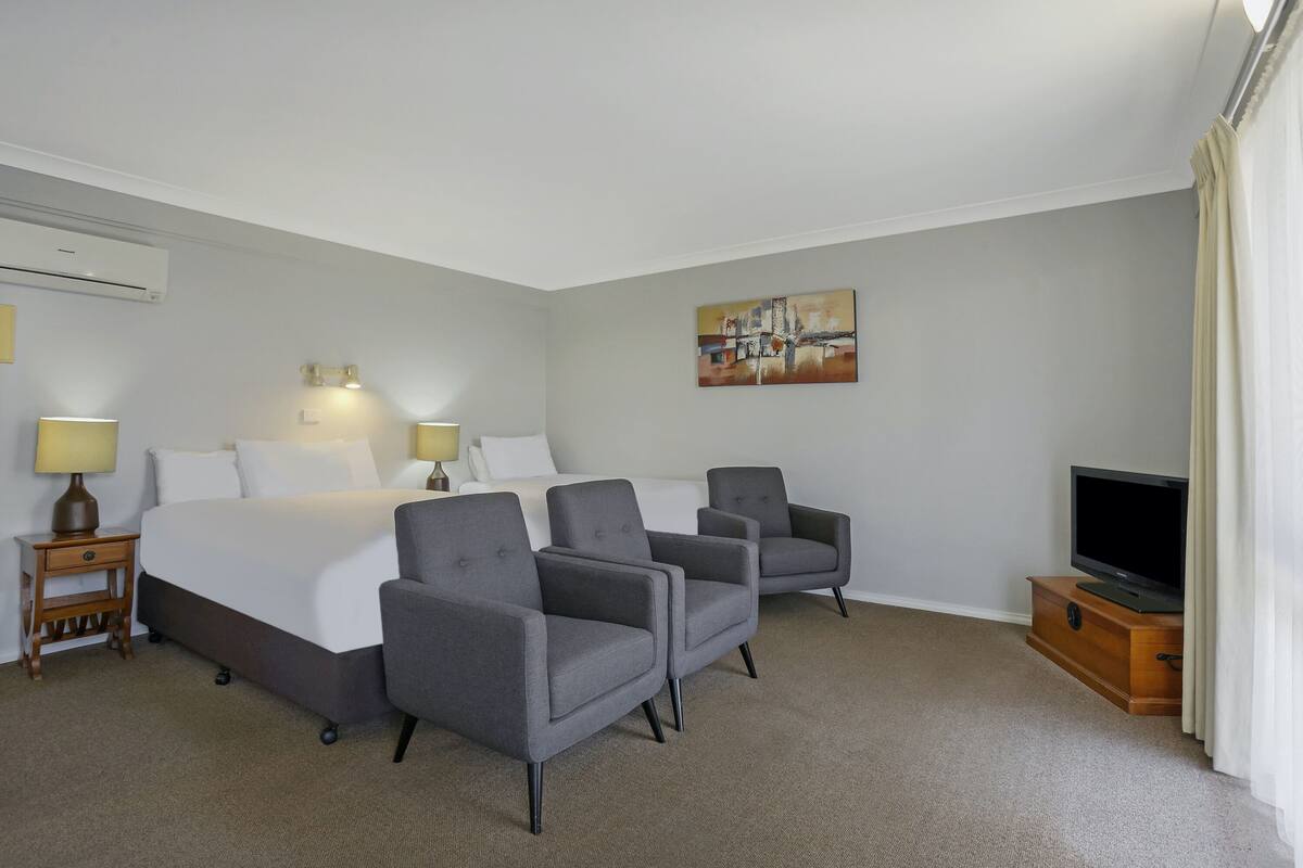 Ein Hotelzimmer mit einem Bett, zwei Sesseln, einem Fernseher und einem Bild an der Wand.